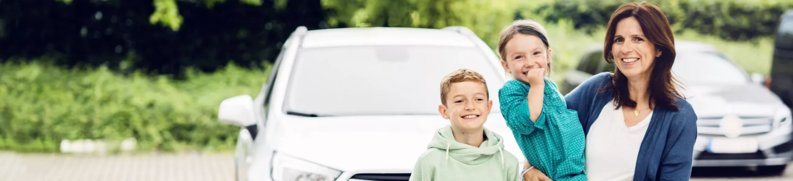 Frau mit zwei Kindern vor einem Auto